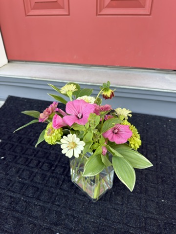 Pink, white, and green garden flowers in a square glass vase at a doorstep