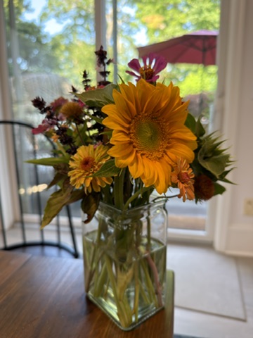 Orange sunflower and burgundy garden flower arrangement in a square vase